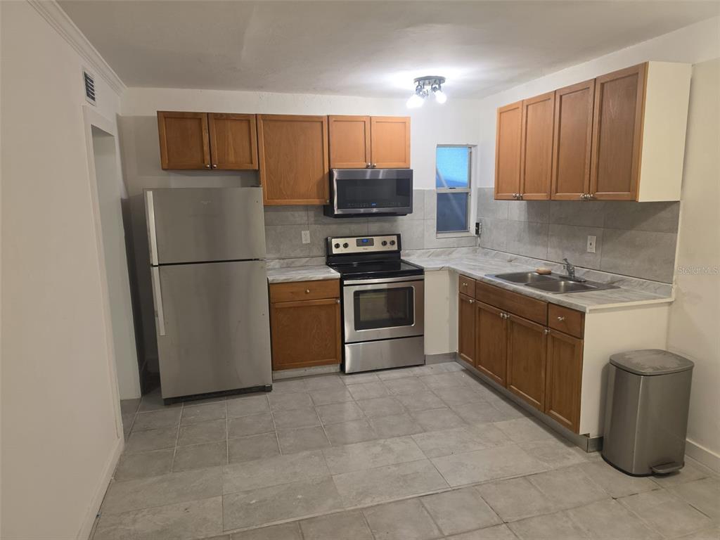 A kitchen features wood cabinets, stainless steel appliances, gray tile flooring, and a marble-look countertop — 1844 JOHN RIVERS STREET UNIT B, SARASOTA, FL