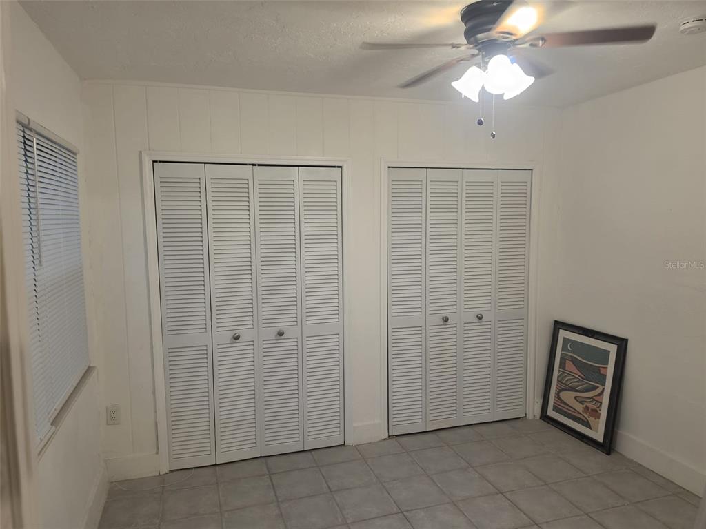A room with white paneled walls, tile flooring, two louvered closet doors, and a ceiling fan — 1844 JOHN RIVERS STREET UNIT B, SARASOTA, FL