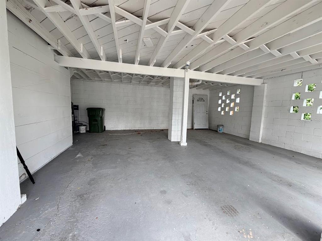 An open-air carport with a concrete floor, white painted block walls, and exposed ceiling joists — 302.5 S 12TH, LEESBURG, FL