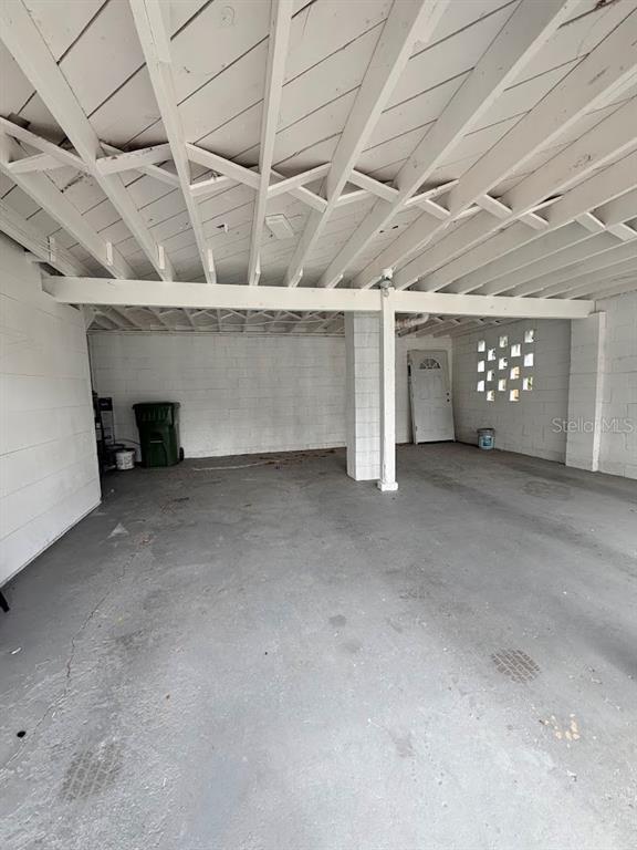 A covered concrete carport features exposed ceiling rafters and white painted block walls — 302.5 S 12TH, LEESBURG, FL