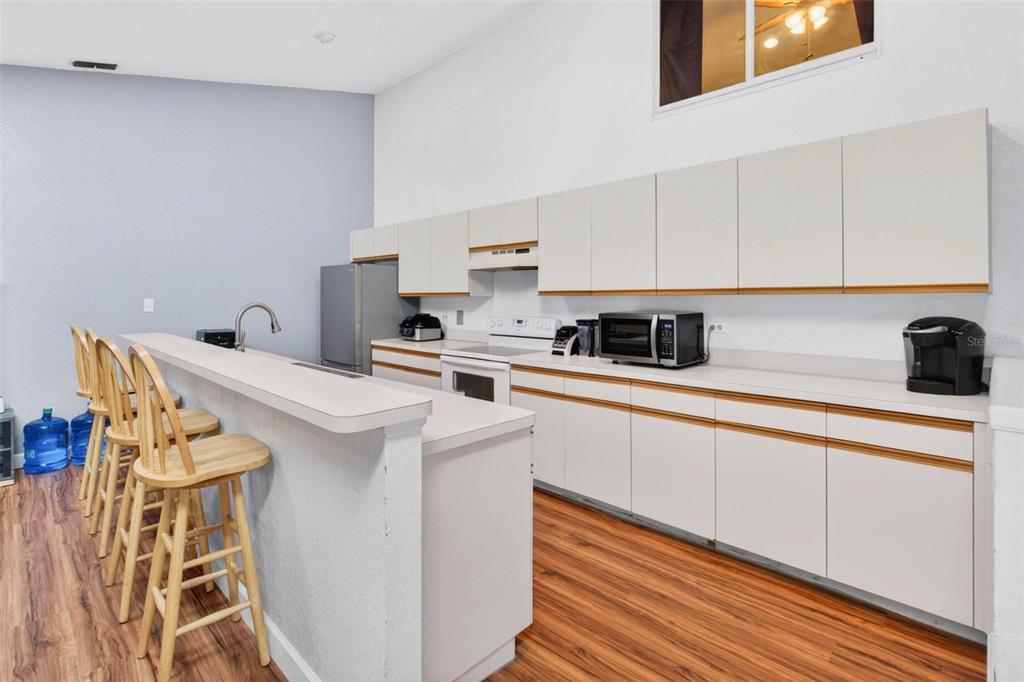 A kitchen features white cabinets, laminate countertops, stainless steel appliances, and wood-look flooring — 6389 93RD TERRACE N UNIT 4706, PINELLAS PARK, FL