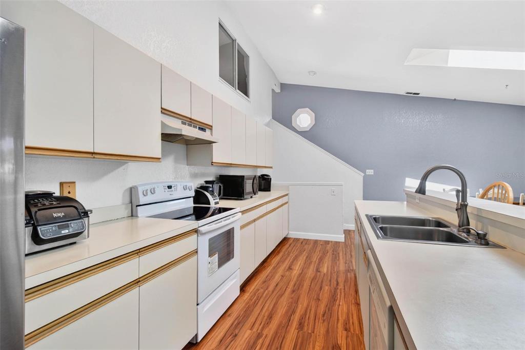 A kitchen with white cabinets and a breakfast bar overlooks a dining area with skylights — 6389 93RD TERRACE N UNIT 4706, PINELLAS PARK, FL