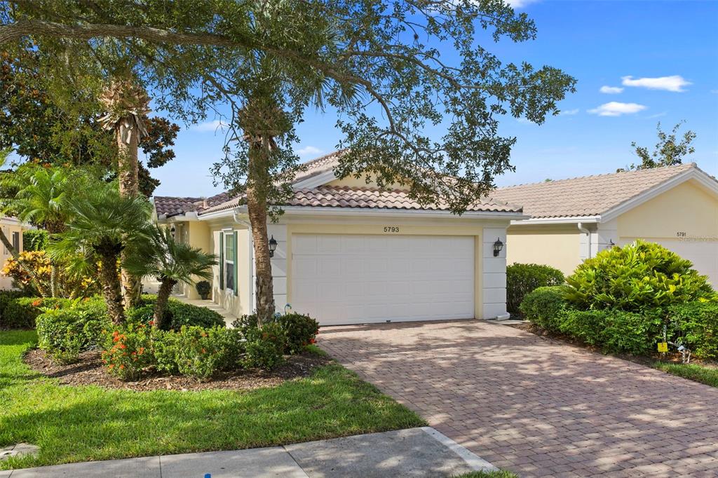 A single-story house with a beige stucco exterior, a tile roof, and a brick driveway — 5793 ITHACA WAY, SARASOTA, FL