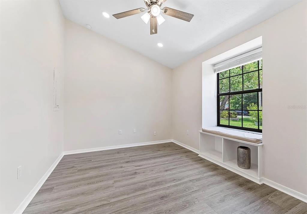An empty room with light-colored walls, wood-look flooring, a ceiling fan, and a window seat — 1302 83RD STREET NW, BRADENTON, FL