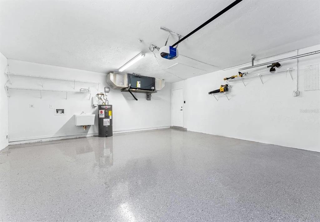 A garage with white walls, a grey epoxy floor, a water heater, and wall-mounted shelving — 1302 83RD STREET NW, BRADENTON, FL