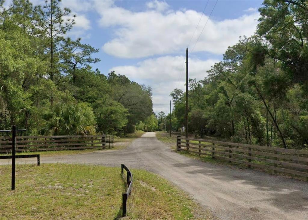 A gravel road leads through a wooded area flanked by wooden fences — Lot 1 NE 127TH STREET, FORT MC COY, FL