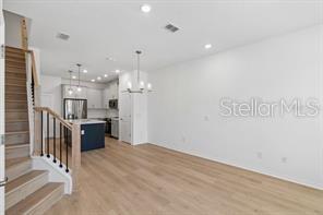 A modern open-concept living area features light wood flooring, a staircase, and a kitchen island — 4345 ROUSH AVENUE, ORLANDO, FL