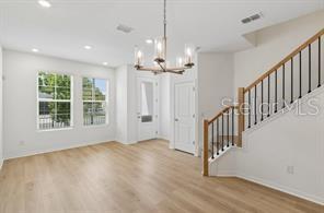 A bright room with light wood flooring, a chandelier, and a staircase with black railings — 4345 ROUSH AVENUE, ORLANDO, FL