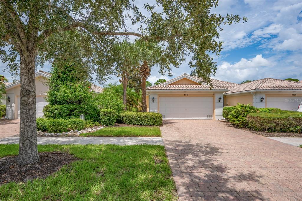 A paved driveway leads to the garage of a single-story house with a tiled roof — 8012 CAMMINARE DRIVE, SARASOTA, FL