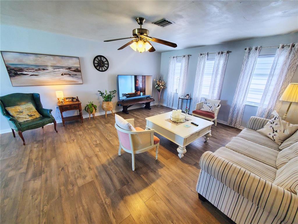 A living room features wood-look flooring, a ceiling fan, a television, and assorted seating furniture — 4 GOLFVIEW ROAD, ROTONDA WEST, FL