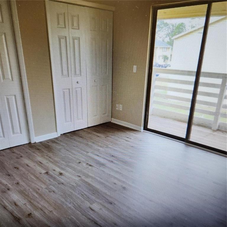 A bedroom with wood-look flooring, white closet doors, and a sliding glass door to a balcony — 22630 GAGE LOOP UNIT 4, LAND O LAKES, FL