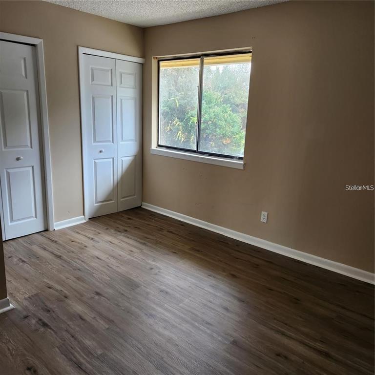 A bedroom with tan walls, wood-look flooring, two white closet doors, and a window — 22630 GAGE LOOP UNIT 4, LAND O LAKES, FL