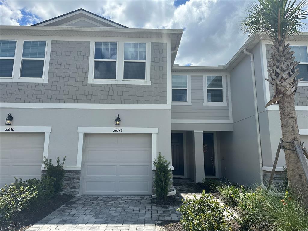 A two-story townhouse exterior features a gray garage, stone accents, and a paved driveway — 26128 FANTASY SKY LANE, LUTZ, FL