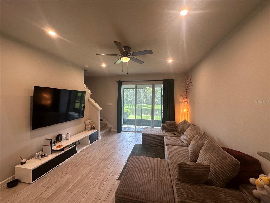 A living room features a large television, a sectional sofa, and sliding glass doors — 26128 FANTASY SKY LANE, LUTZ, FL