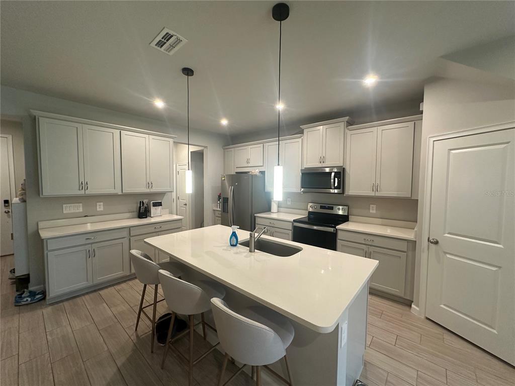A modern kitchen features light gray cabinets, white countertops, a central island, and stainless steel appliances — 26128 FANTASY SKY LANE, LUTZ, FL