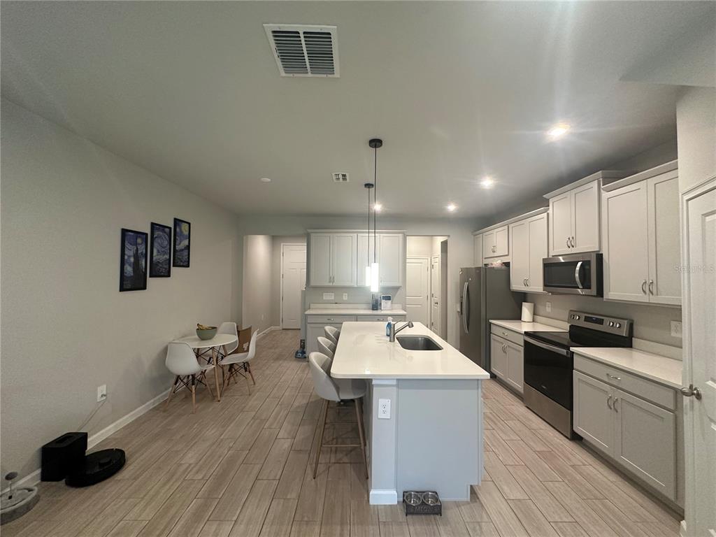 A modern kitchen features light gray cabinetry, a central island with bar seating, and tile flooring — 26128 FANTASY SKY LANE, LUTZ, FL