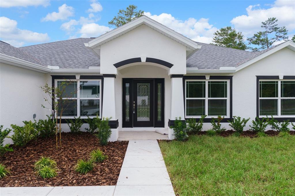 The exterior of a white house features a dark front door and black window trim — 13058 KITTIWAKE ROAD, WEEKI WACHEE, FL