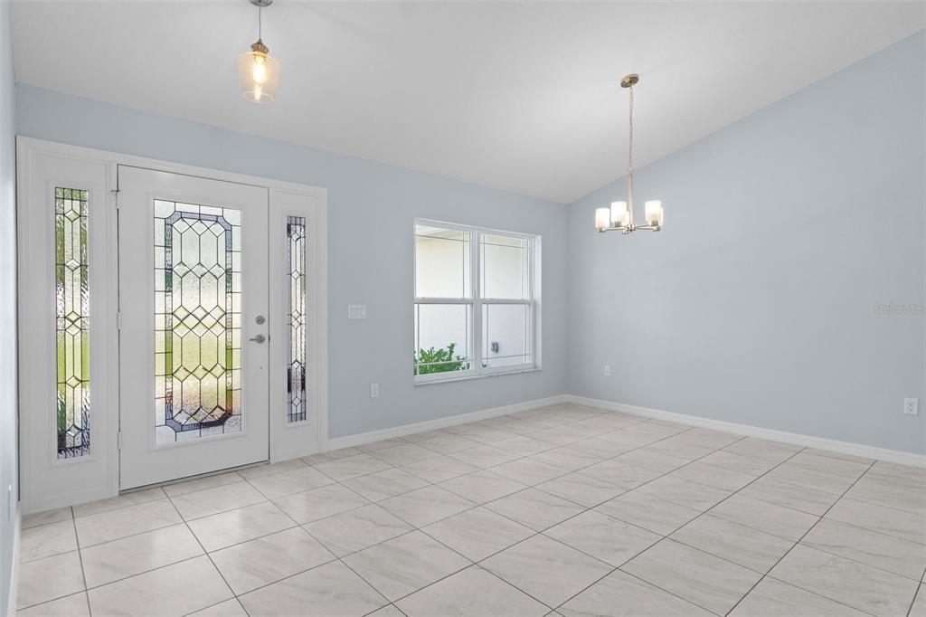 An empty dining room with light blue walls, tile flooring, and a decorative glass front door — 13058 KITTIWAKE ROAD, WEEKI WACHEE, FL