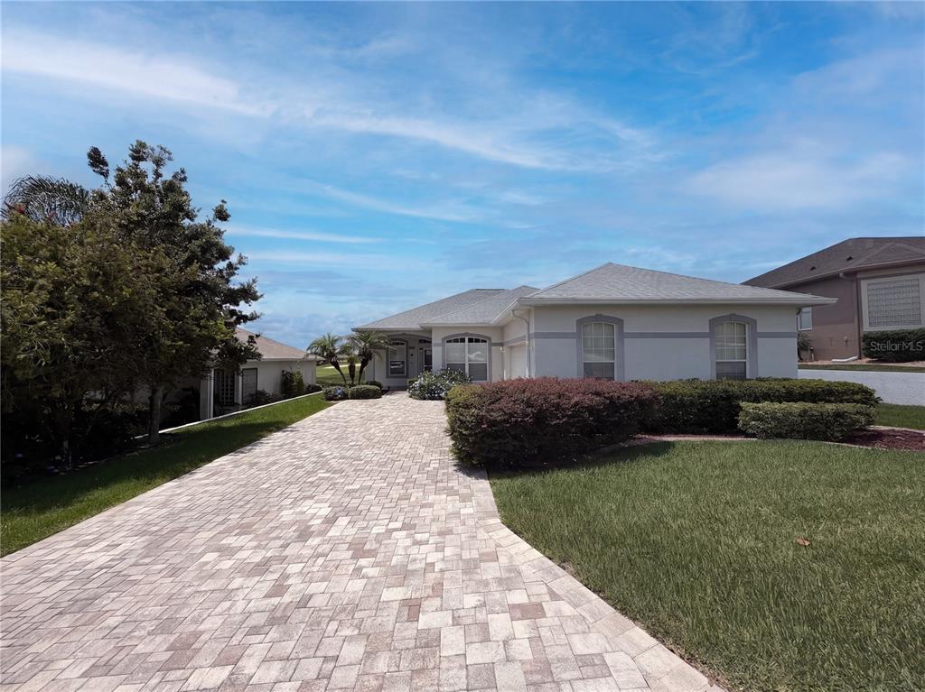 A single-story house with a paved driveway and landscaped front yard under a blue sky — 11734 SE 173RD LANE ROAD, SUMMERFIELD, FL