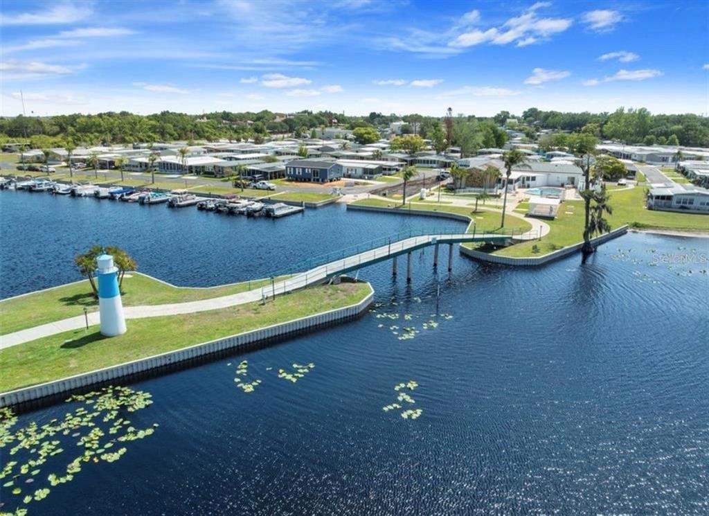 An aerial view shows a pedestrian bridge connecting a grassy point to a waterfront community — 1401 W HIGHWAY 50 UNIT 179, CLERMONT, FL