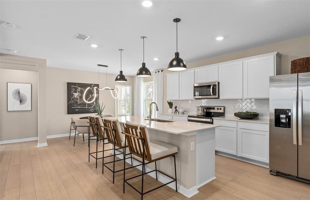 A modern kitchen features white cabinetry, a central island with bar seating, and stainless appliances — 6902 CREEK FALLS ALLEY, CLERMONT, FL
