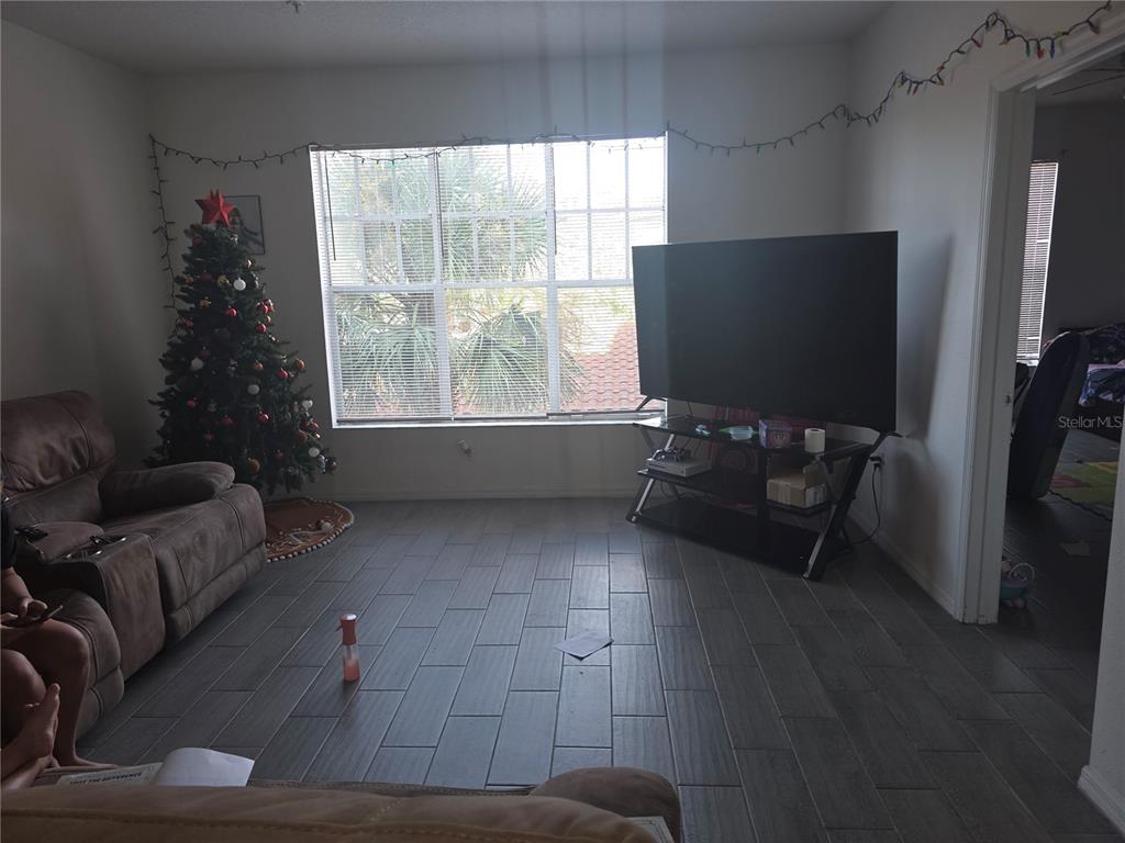 A living room features gray tile flooring, a large window, a television, and a Christmas tree — 5554 METROWEST BOULEVARD UNIT 206, ORLANDO, FL