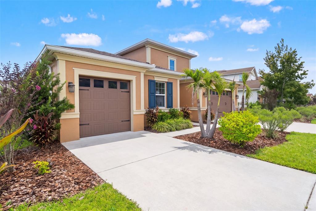 A tan house exterior features a brown garage door, blue shutters, and a concrete driveway — 1723 WHITEWILLOW DRIVE, WESLEY CHAPEL, FL