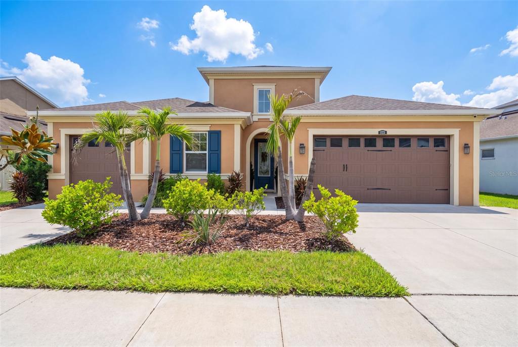 A single-story house with a tan stucco exterior, blue shutters, and a three-car garage — 1723 WHITEWILLOW DRIVE, WESLEY CHAPEL, FL