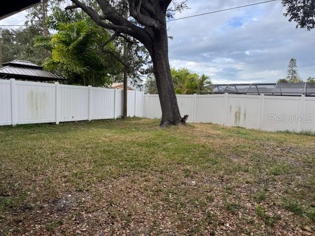 A grassy backyard features a large tree and a white vinyl privacy fence — 1815 2ND AVENUE E, BRADENTON, FL