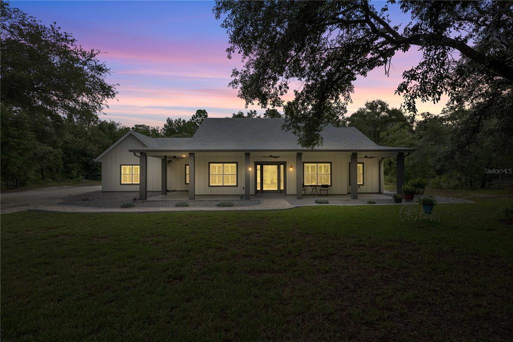 A single-story house with a covered front porch and board-and-batten siding at sunset — 18272 SW 65TH LOOP, DUNNELLON, FL