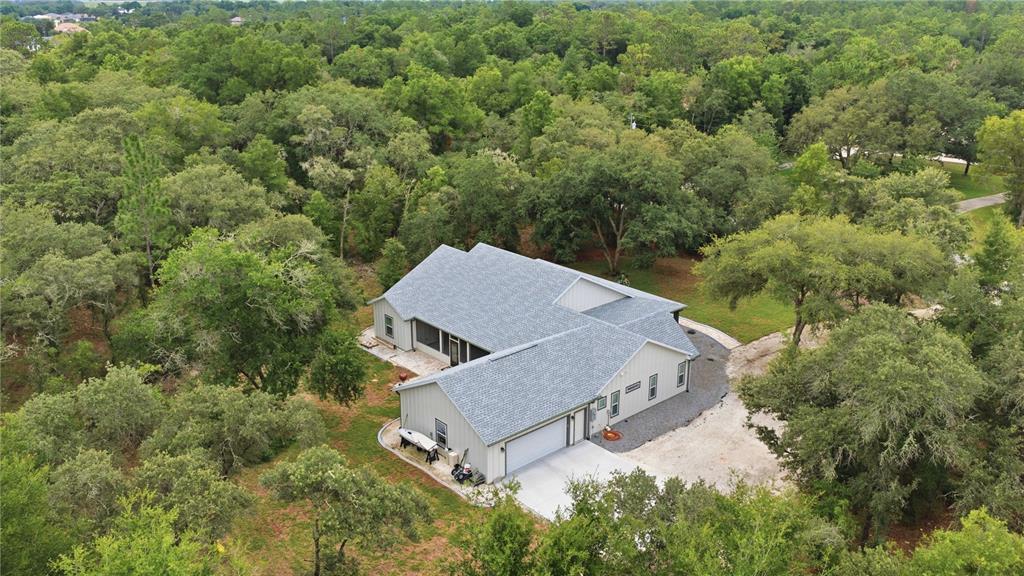 An aerial view of a light-colored house with a gray roof surrounded by dense trees — 18272 SW 65TH LOOP, DUNNELLON, FL
