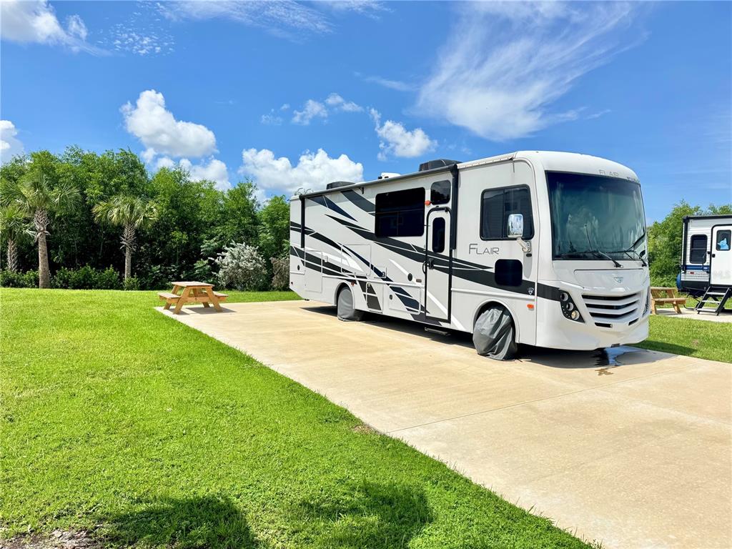 A white and black Flair motorhome is parked on a concrete pad in a grassy area — 240 HORIZON ROAD, PUNTA GORDA, FL