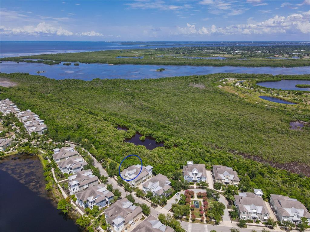 An aerial view shows a residential neighborhood surrounded by dense green forest and coastal waters — 311 SAPPHIRE LAKE DRIVE UNIT 202, BRADENTON, FL