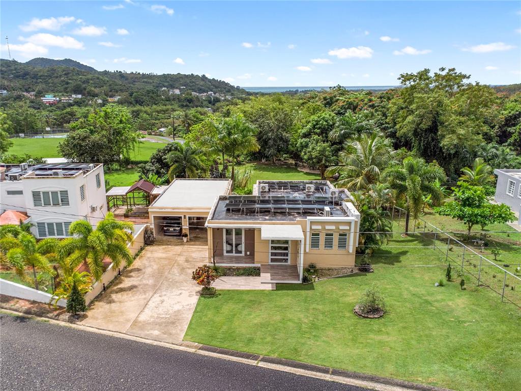 An aerial view shows a tan house with solar panels, a garage, and a large lawn — PR 757 KM 1.7 INT LOT 4 LA CEIBA POLLOS WARD, PATILLAS, PR
