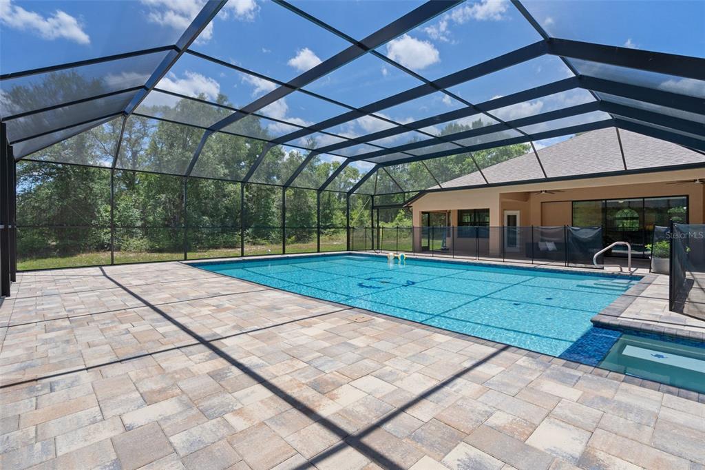 A screened-in swimming pool with a paver deck sits behind a house near trees — 222 SUNCOAST BOULEVARD, SPRING HILL, FL