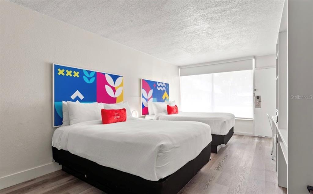 A hotel room features two beds with colorful headboards, white bedding, and light wood flooring — 2930 NE POLYNESIAN ISLE UNIT 219, KISSIMMEE, FL
