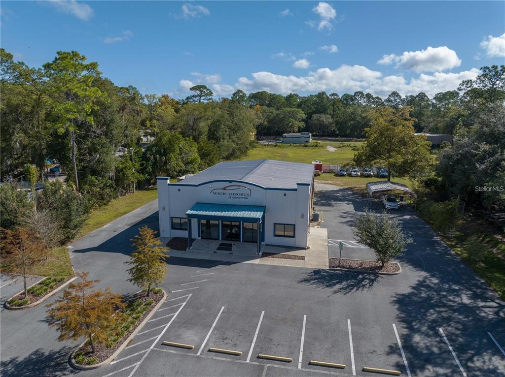 An aerial view shows a commercial building with a parking lot and surrounding trees — 1725 N MAIN STREET, GAINESVILLE, FL