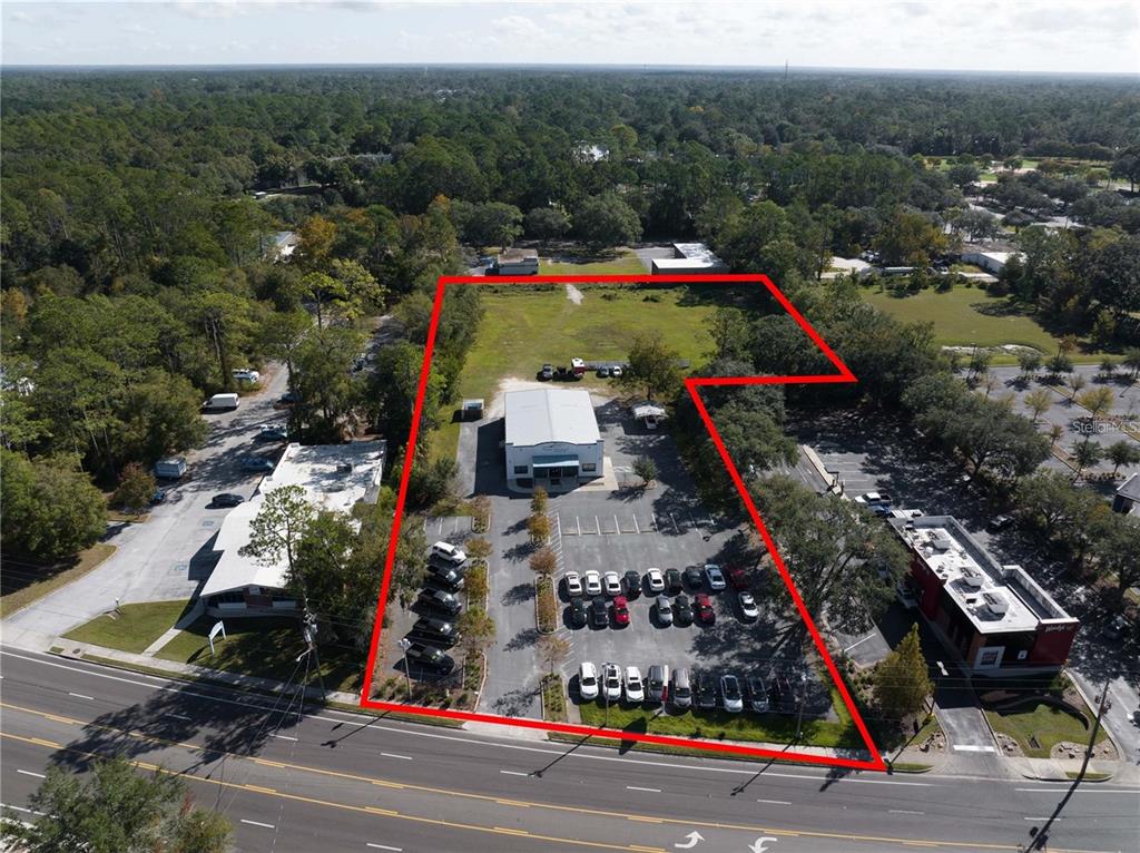 An aerial view shows a commercial property with a building, parking lot, and grassy area — 1725 N MAIN STREET, GAINESVILLE, FL