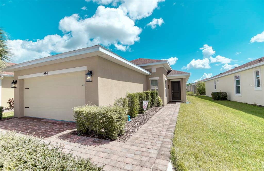 The exterior of a tan, single-story house features a two-car garage and a paved walkway — 284 VESTRELLA DRIVE, POINCIANA, FL
