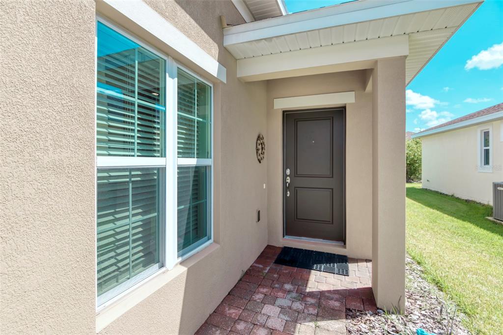 A tan stucco house exterior features a dark brown front door and a brick walkway — 284 VESTRELLA DRIVE, POINCIANA, FL