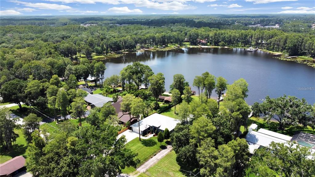 An aerial view shows a house with a white roof situated near a large lake — 17017 PAULA LANE, LUTZ, FL