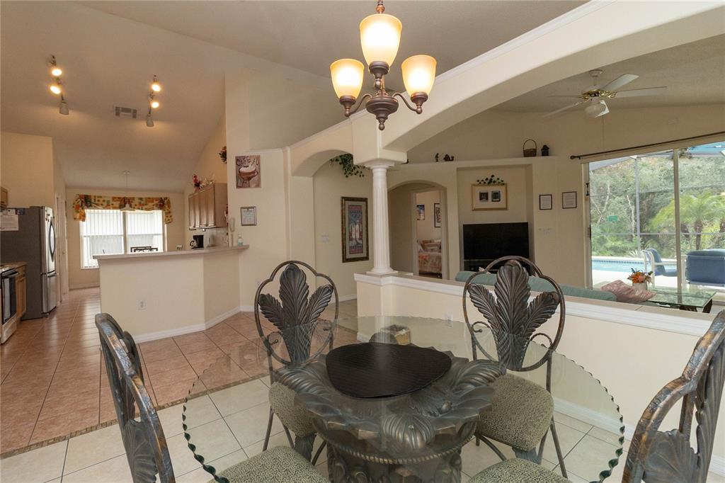 A dining area with a glass table and chairs overlooks a kitchen and living room — 4626 EAGLE PEAK DRIVE, KISSIMMEE, FL