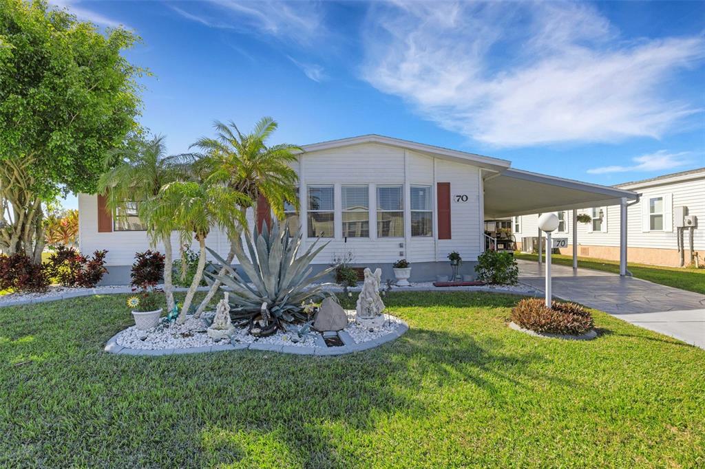 A single-story manufactured home with white siding, a carport, and a landscaped front yard — 70 MOCKINGBIRD LANE, ELLENTON, FL