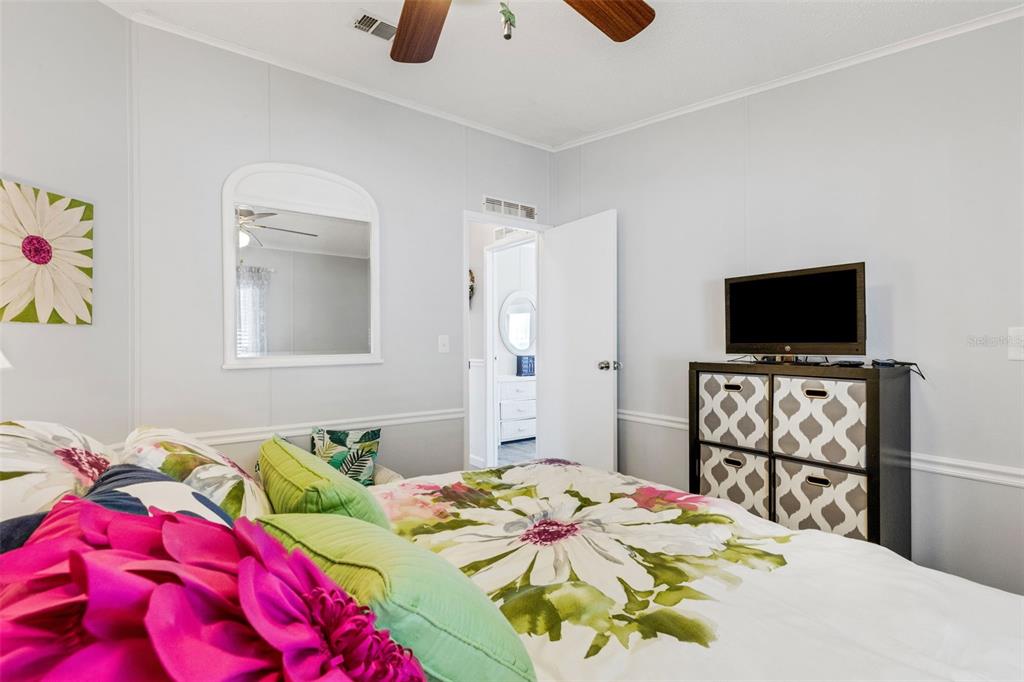 A bedroom features a bed with floral bedding, a dresser with a television, and a mirror — 70 MOCKINGBIRD LANE, ELLENTON, FL