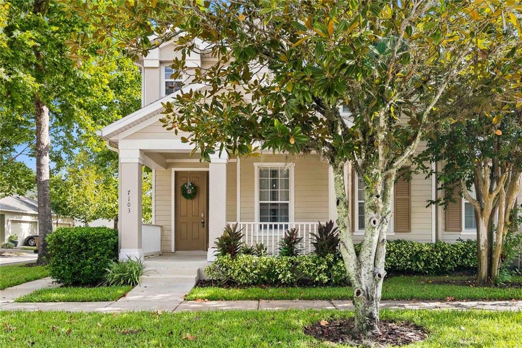 A two-story house with beige siding, a covered front porch, and a landscaped front yard — 7103 RED LANTERN DRIVE UNIT 7103, HARMONY, FL