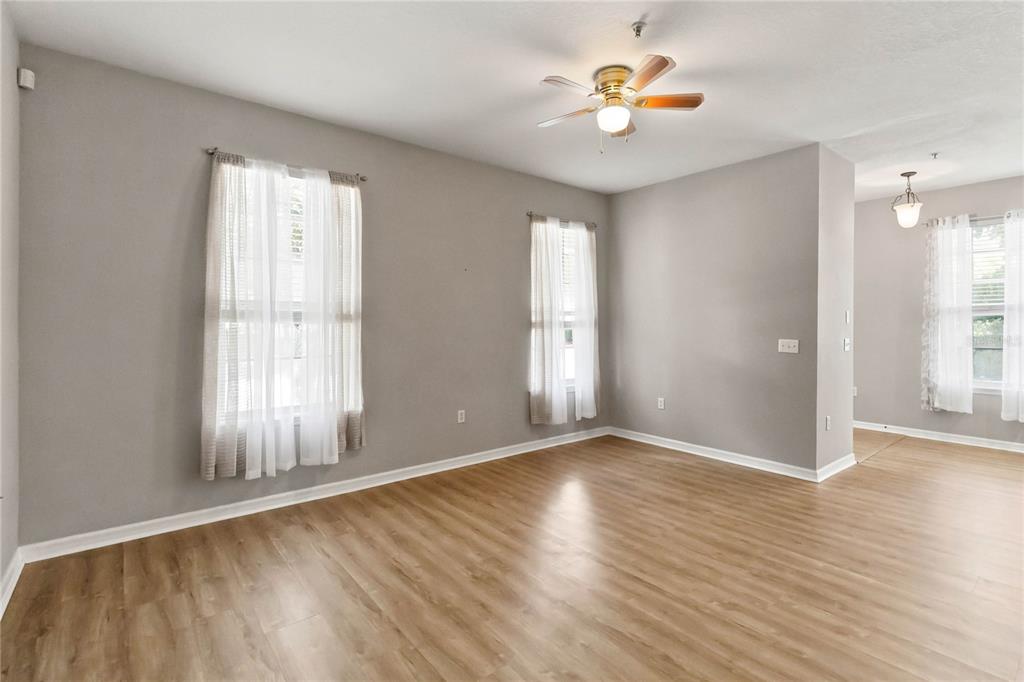 An empty room with light wood-look flooring, gray walls, three windows, and a ceiling fan — 7103 RED LANTERN DRIVE UNIT 7103, HARMONY, FL