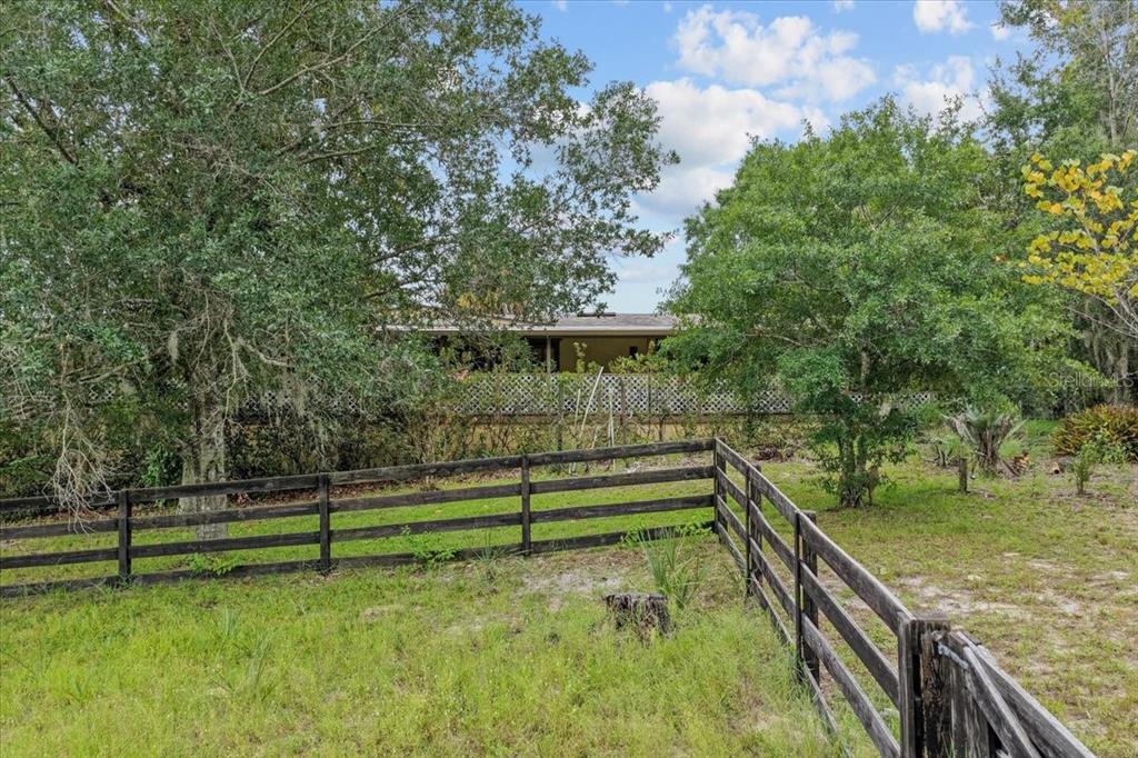 A paved driveway leads through an open metal gate flanked by stone pillars and trees — 470 FAY AVENUE, SPRING HILL, FL