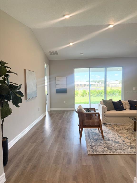 A living room with light wood floors, a gray sofa, and a view of the backyard — 4329 CREMONA DRIVE, SEBRING, FL