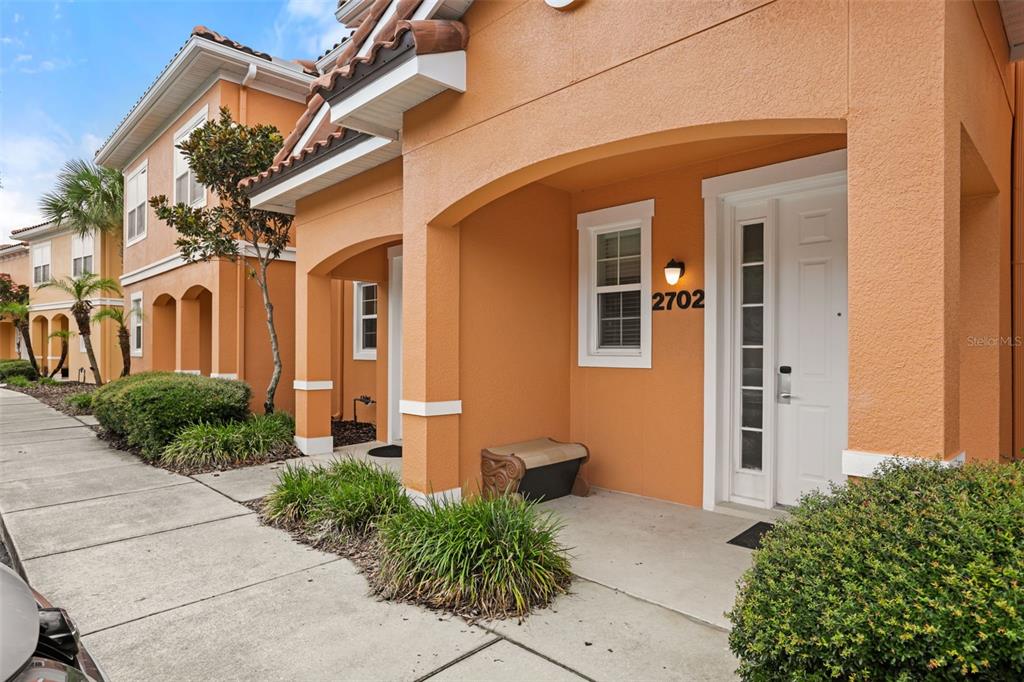 An exterior view of a two-story orange stucco townhouse complex with a parking lot — 2702 CORVETTE LANE, KISSIMMEE, FL