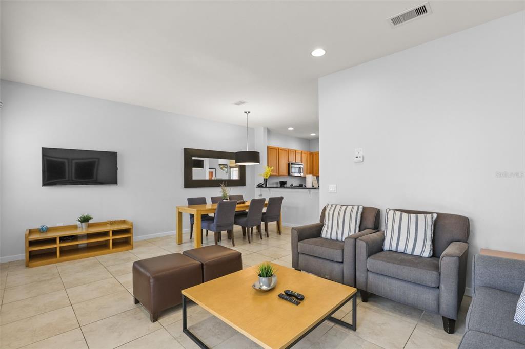 An open-concept living and dining area features tile flooring, neutral walls, and modern furniture — 2702 CORVETTE LANE, KISSIMMEE, FL